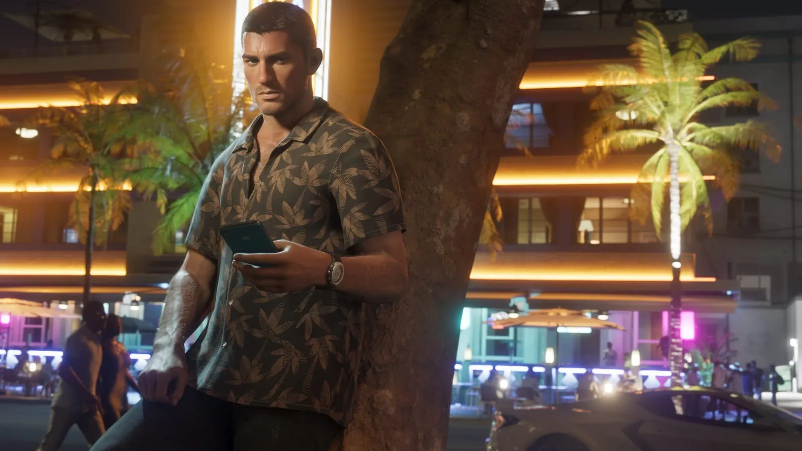 Homme en chemise à motifs consultant son téléphone la nuit, façade d'hôtel éclairée derrière lui