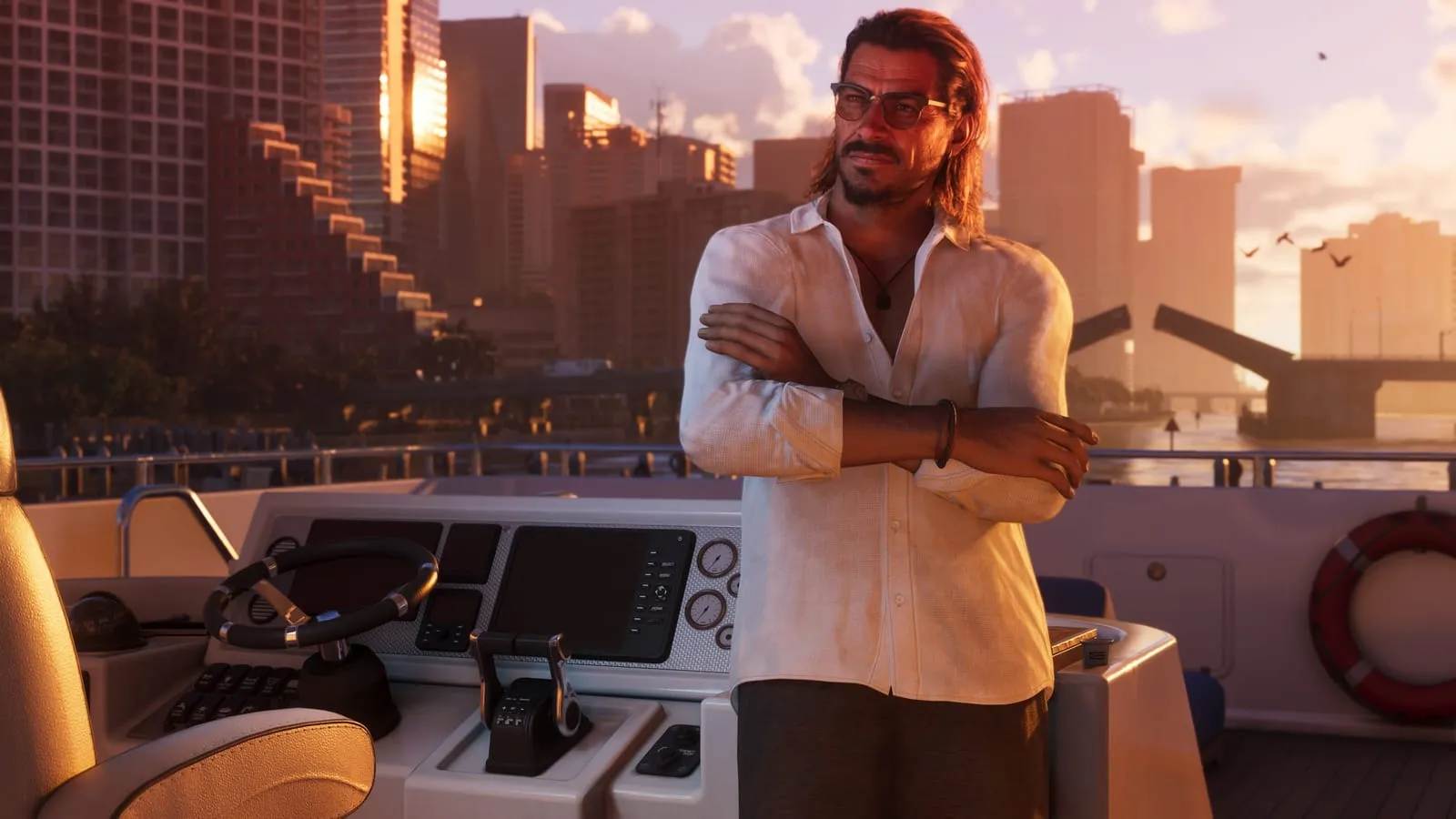Man in a white shirt stands arms crossed on a boat as the city skyline glows at sunset