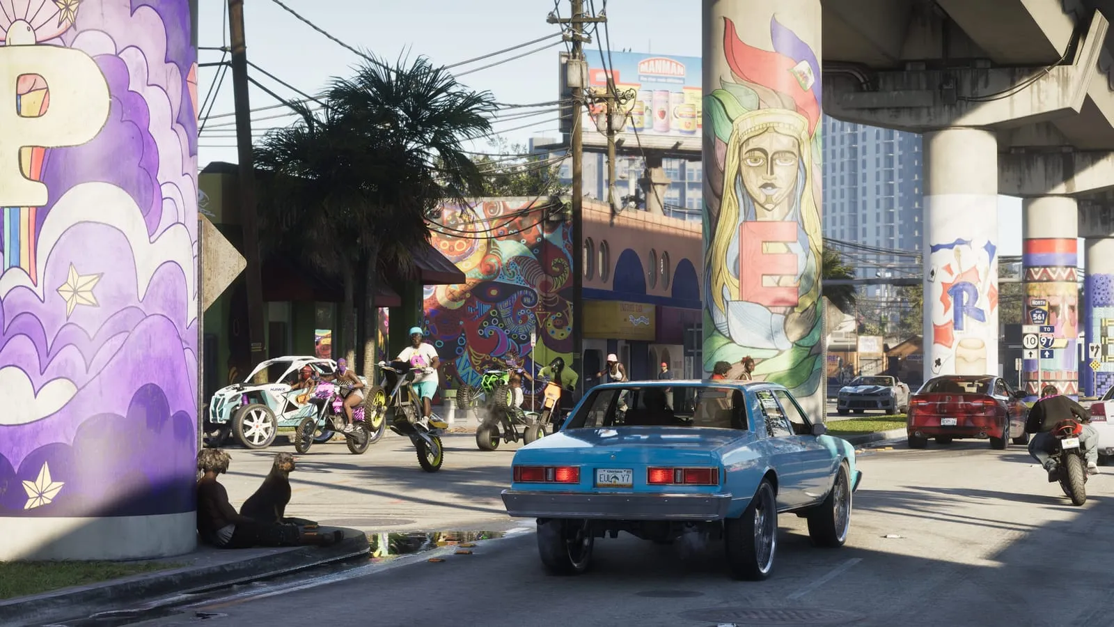 A blue lowrider and wheelie riders under highway pillars painted with murals